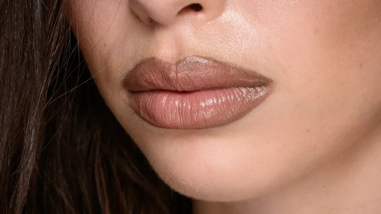 Labbra carnose e lucide, con un effetto naturale per ingrandire le labbra, evidenziate da un rossetto nude.