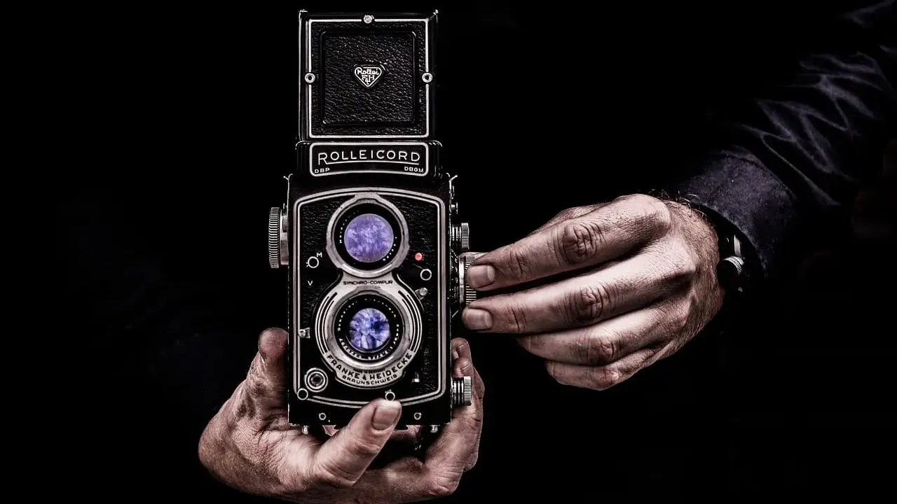 Dwie ręce trzymają aparat Rolleiflex, jedna reguluje ostrość. Sztuka fotografii, zasada złotego środka w kadrze.