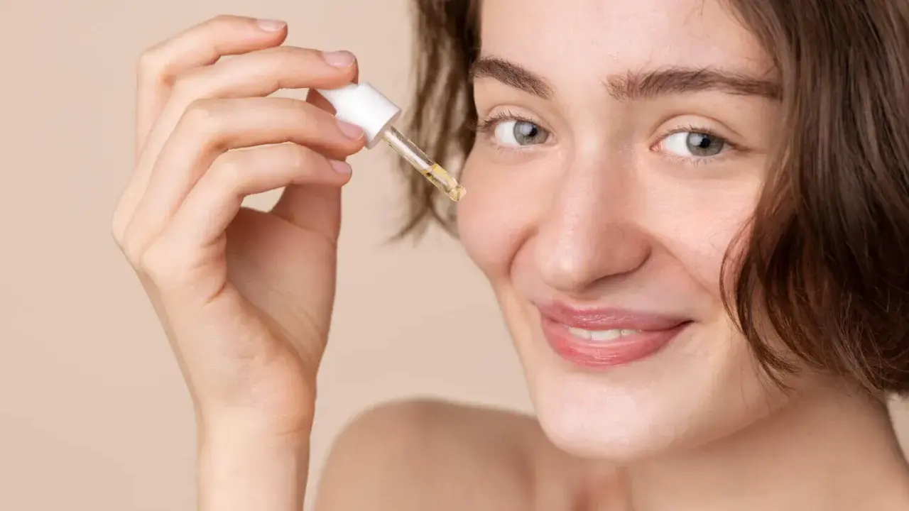 Une femme souriante applique une goutte de sérum à la vitamine C sur son visage. C'est le moment idéal pour utiliser la vitamine C sur le visage pour une peau éclatante.