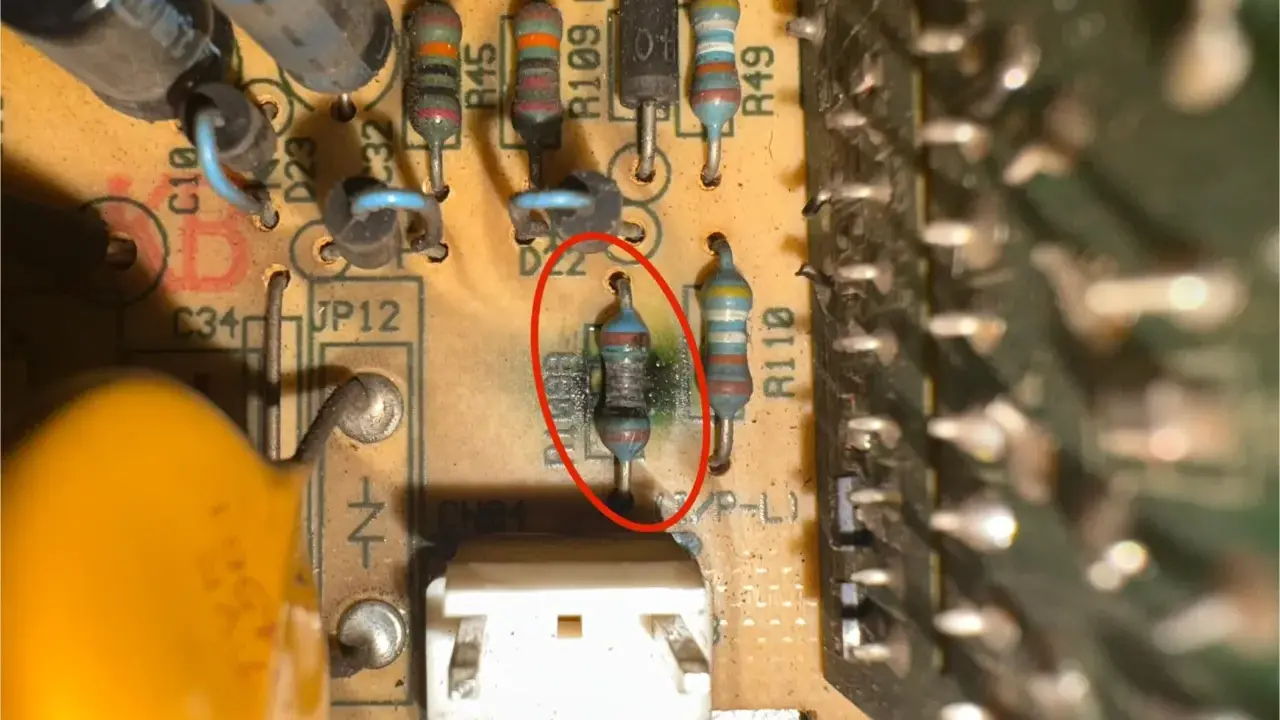 Uszkodzony opornik z czerwonym okręgiem na płytce drukowanej, obok innych elementów elektronicznych.