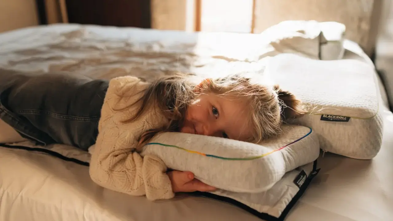 Ein kleines Mädchen kuschelt sich auf einem Bett an ein Kissen. Die Schlafphasen von Kindern sind wichtig für ihre Entwicklung.