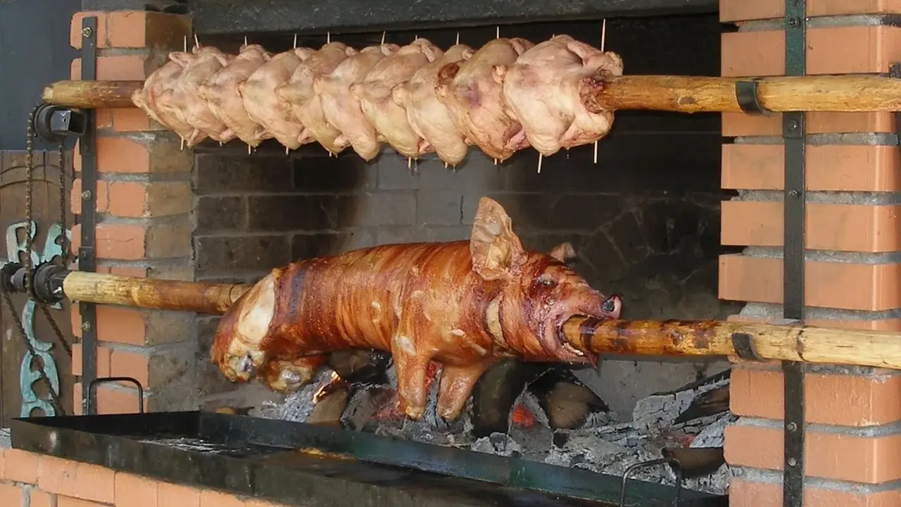 Ein Spanferkel grillen über offenem Feuer. Darüber hängen mehrere Hähnchen am Spieß.