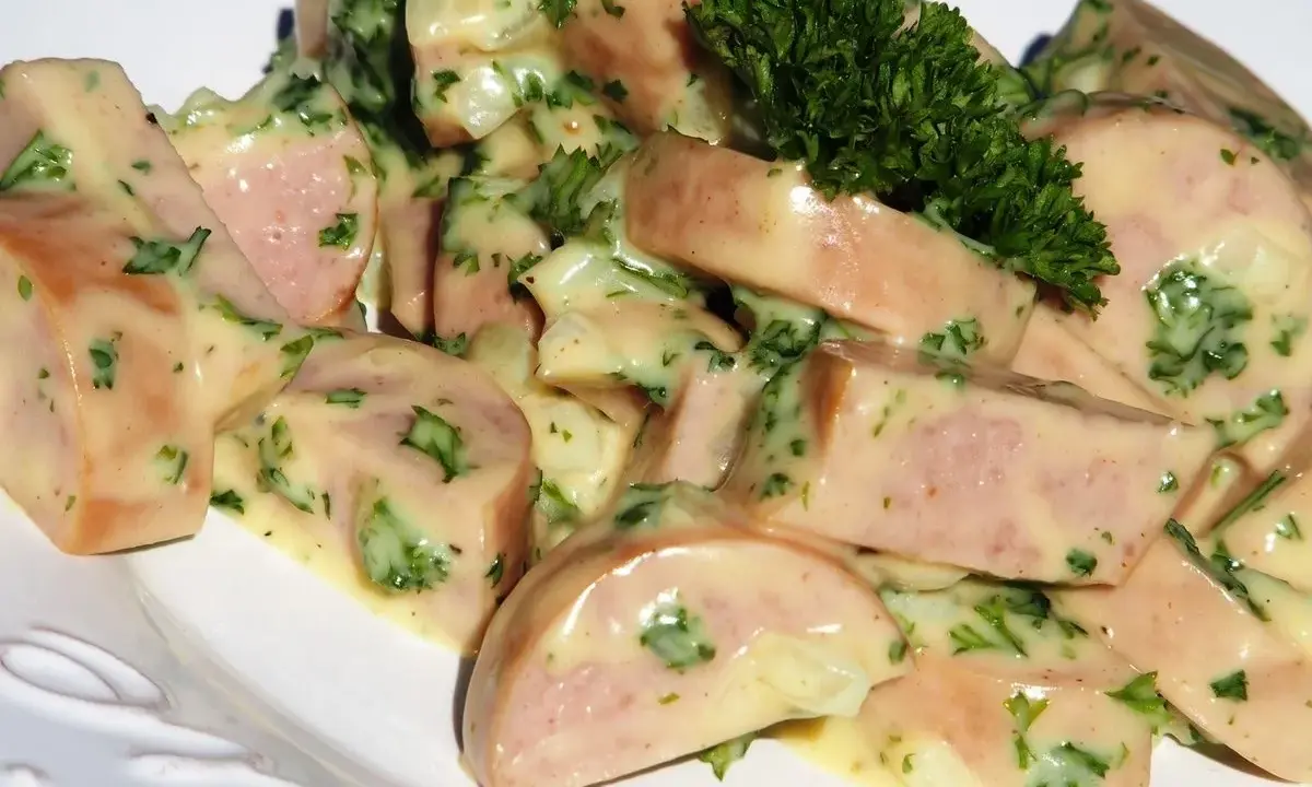 Une délicieuse salade de cervelas, coupée en dés et nappée d'une sauce crémeuse aux herbes fraîches, garnie d'un brin de persil.