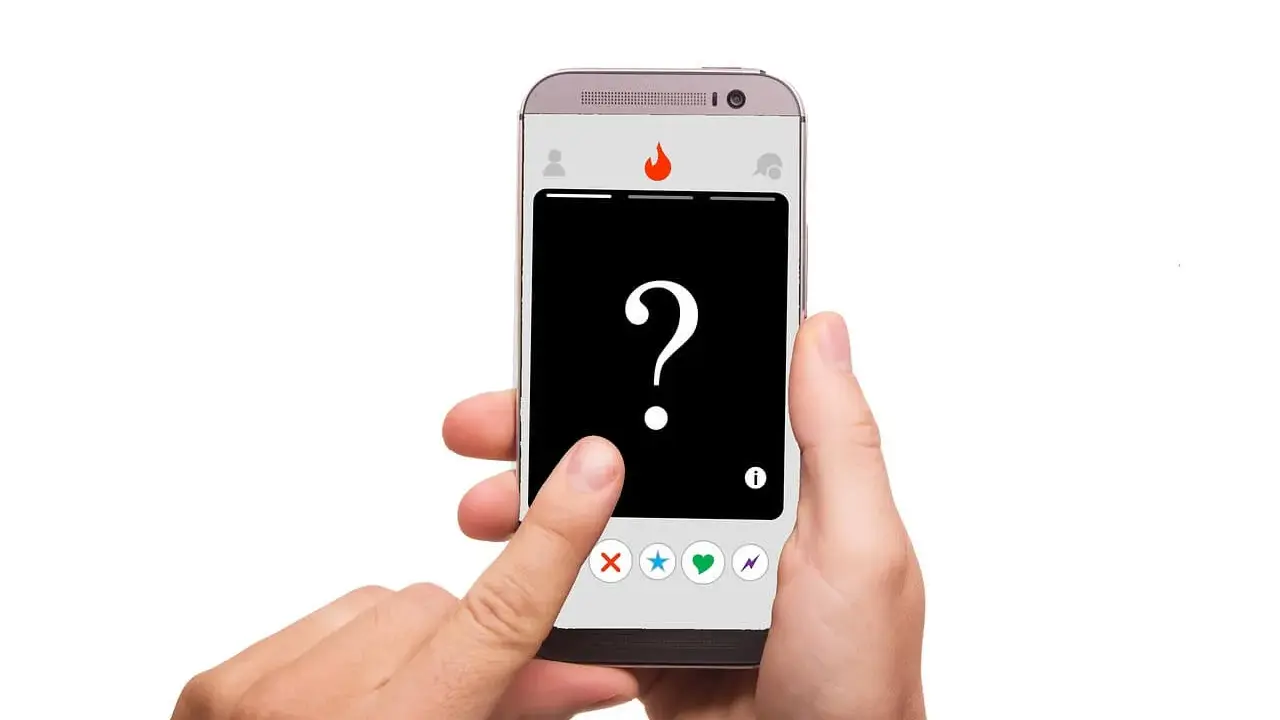 Dłoń trzyma smartfon z aplikacją randkową. Na ekranie znak zapytania i ikony: X, gwiazdka, serce, błyskawica – typowe oznaczenia na Tinderze.