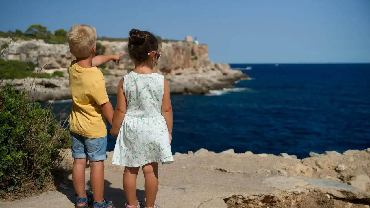 Två barn står vid havet, redo för sommarlåtar och skolavslutning. Pojken pekar mot horisonten.