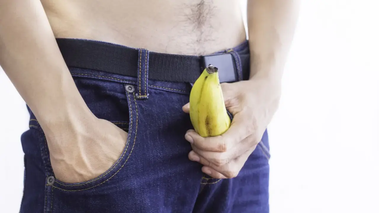 Mężczyzna w dżinsach trzyma banana, sugerując jelqing efekty.