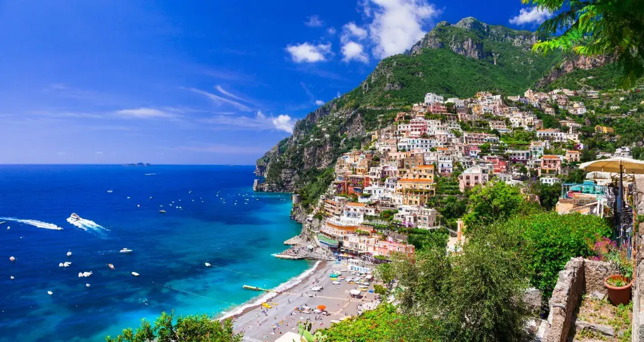 Positano, un gioiello incastonato tra il verde dei monti e l'azzurro del mare in Campania. Case colorate a picco sul mare, una spiaggia affollata e barche che solcano le acque cristalline.
