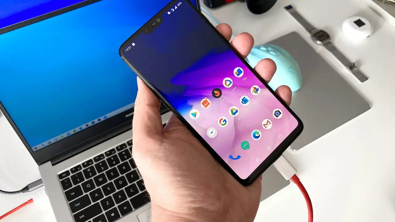 Dłoń trzyma smartfon podłączony kablem do laptopa.