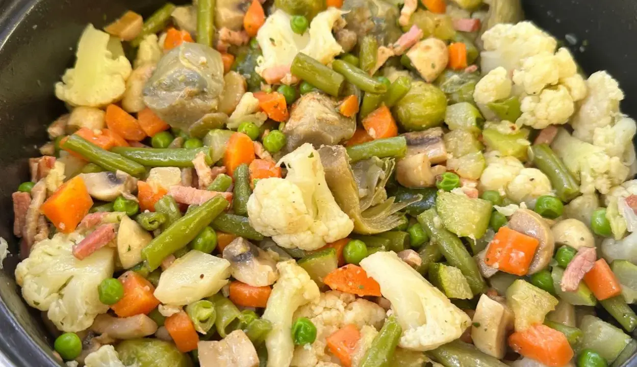 Un plato abundante de menestra de verduras, con brócoli, zanahoria, judías verdes, guisantes y trozos de tocino.