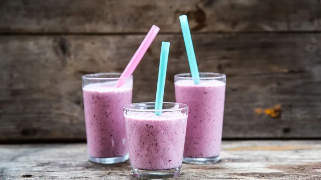 Tre glas med lila smoothie, perfekta för ett snabbt smoothie recept. Blå och rosa sugrör sticker upp.