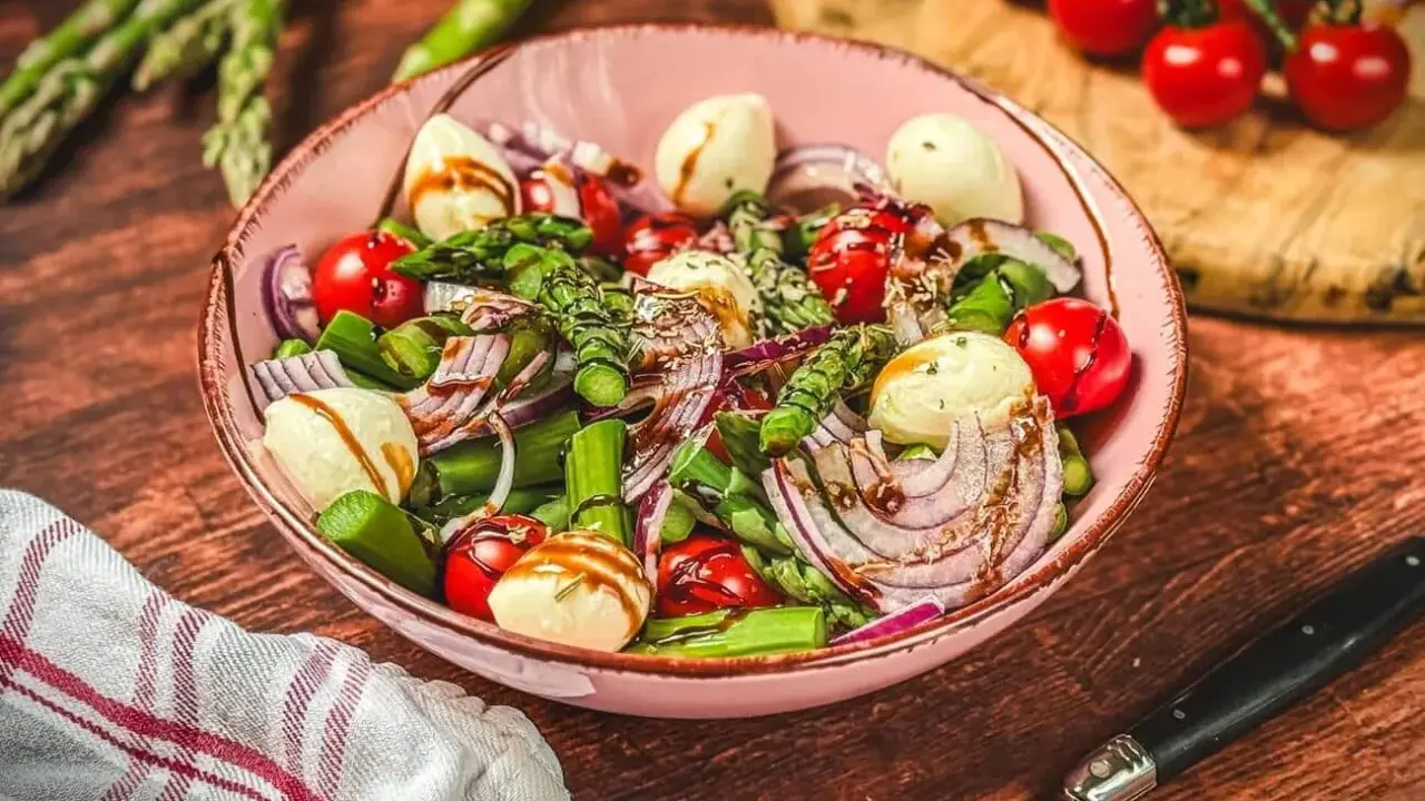 Frischer Spargelsalat mit Ei, Tomaten, roten Zwiebeln und Mozzarella-Kugeln, beträufelt mit Balsamico-Dressing.