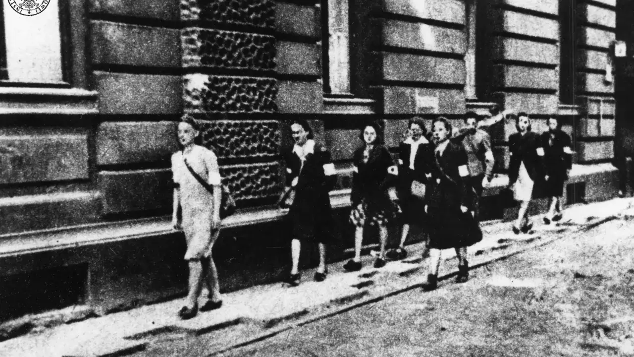 Kobiety w powstaniu warszawskim, idące ulicą. Na ramionach mają opaski.