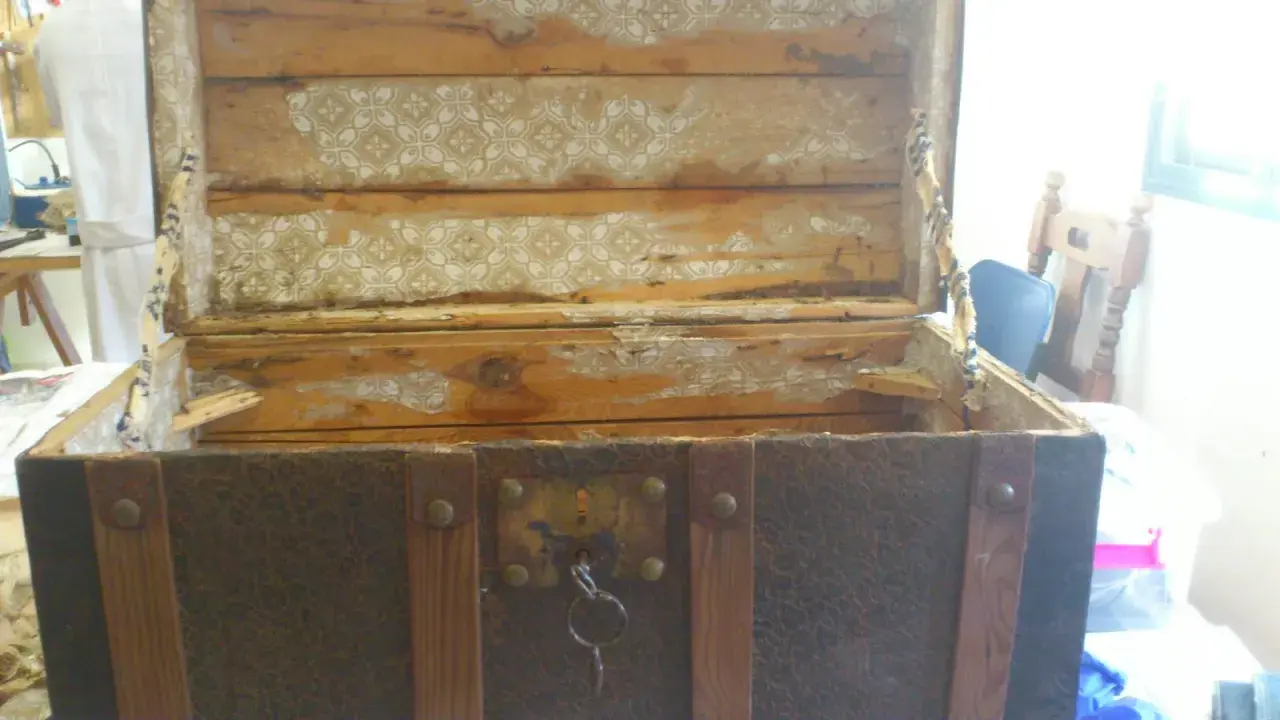 Proceso de restaurar baúl antiguo de chapa y madera. El interior muestra madera desgastada y papel tapiz despegado.