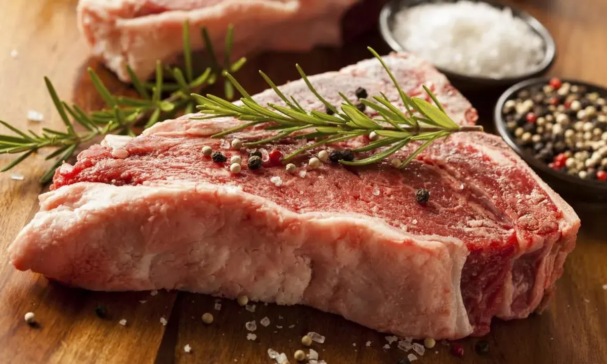 Bistecca alla fiorentina, un cibo succulento pronto per essere cucinato, con rosmarino, sale grosso e pepe.