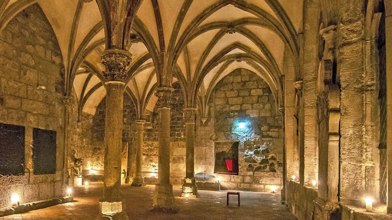 Gewölbte Gänge in einem **kloster mittelalter**. Säulen tragen das steinerne Dach, Kerzenlicht erhellt den Boden.