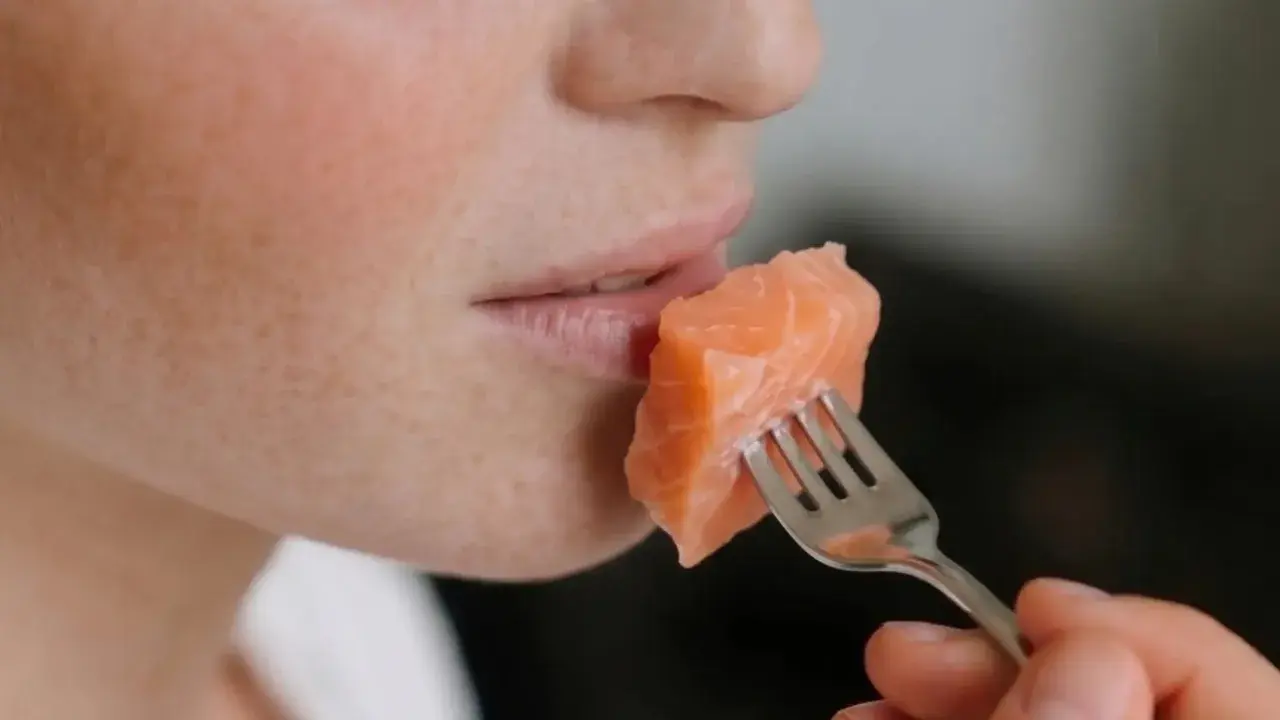 Une personne mange un morceau de saumon à la fourchette. Un aperçu de son visage, idéal pour un avis sur le régime Natman.