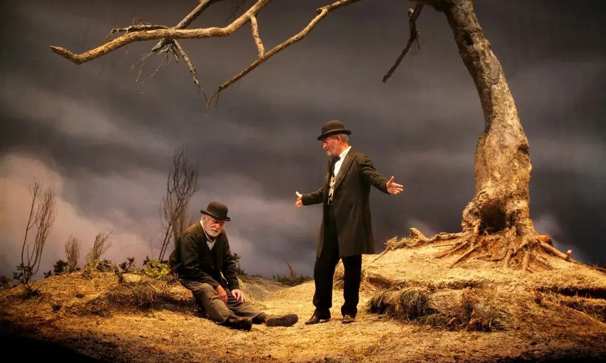 Due uomini, forse Vladimir ed Estragon, attendono Godot sotto un albero spoglio.