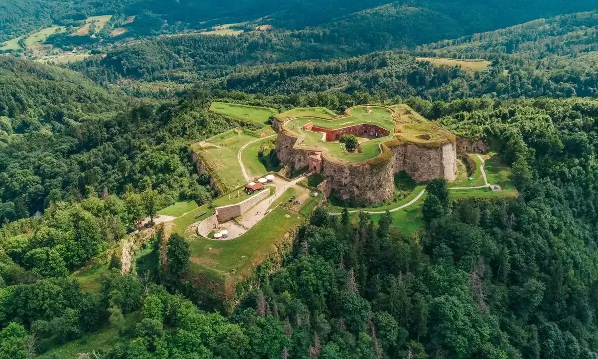 Forteca na zielonym wzgórzu, niczym srebrna góra otoczona lasem, wita zwiedzających.