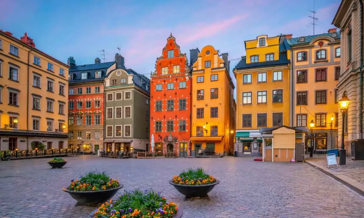Färgglada hus på ett kullerstens torg i Gamla Stan, Stockholm, med blomkrukor i förgrunden.