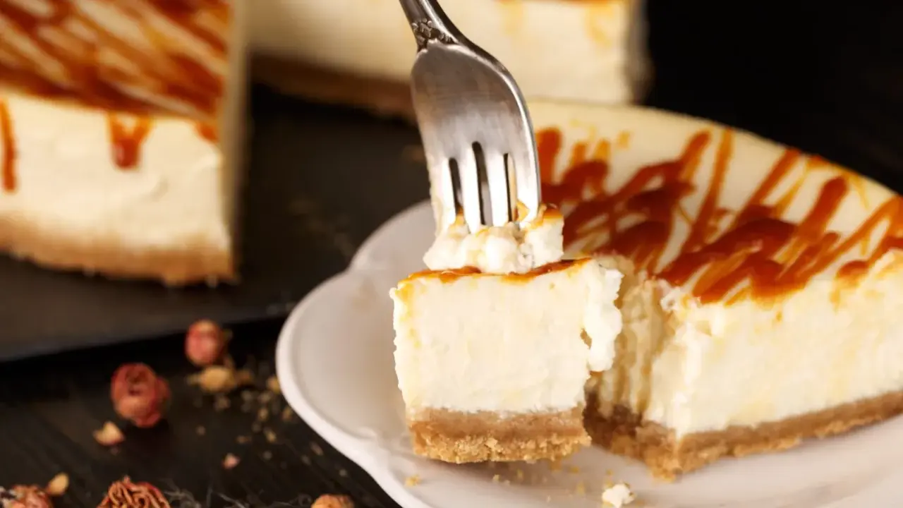 Une fourchette prélève un morceau crémeux de cheesecake, révélant le fromage frais onctueux sous un filet de caramel.