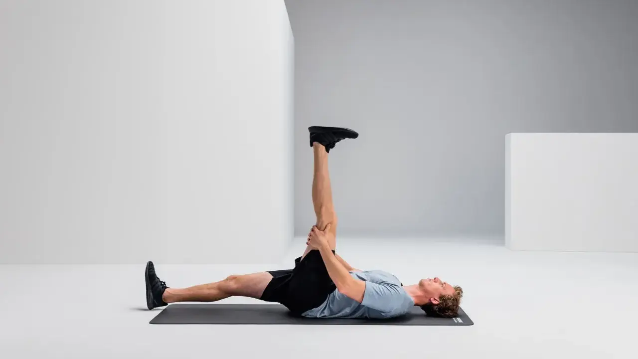 Mann liegt auf Matte, dehnt Bein für Hamstring Training.