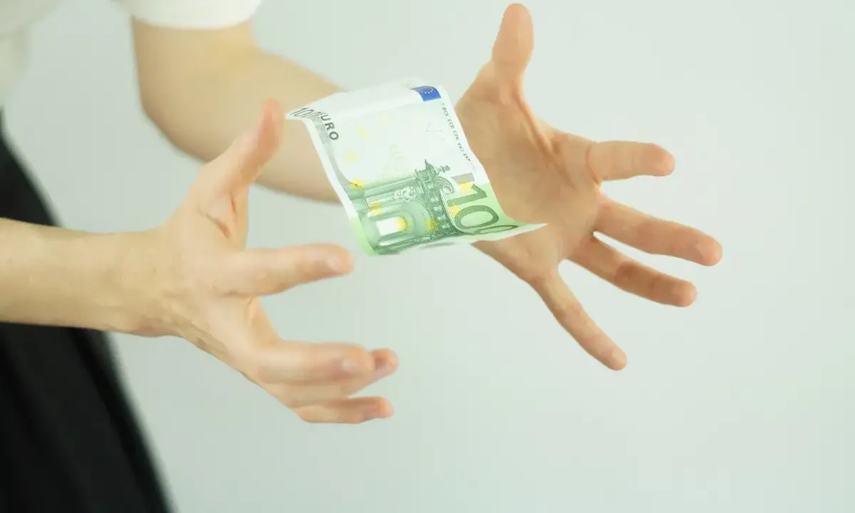 Hände fangen einen 100-Euro-Schein, der schwebt. Ein Symbol für ein Leben ohne Geld, das vielleicht doch möglich ist.