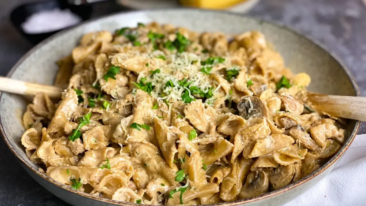 En krämig kyckling svamp pasta i en skål, toppad med persilja och parmesan.