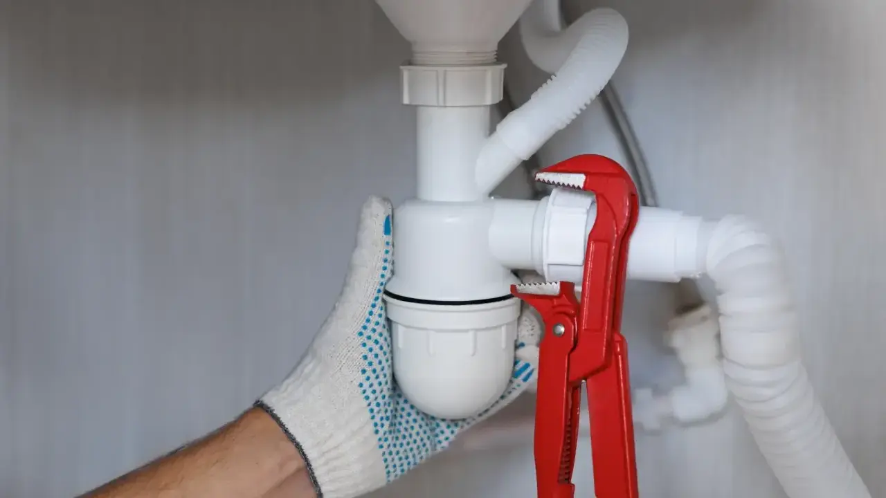 Ręka w rękawicy dokręca kluczem hydrauliczny syfon samoczyszczący, co znaczy, że zapobiega on zatorom.
