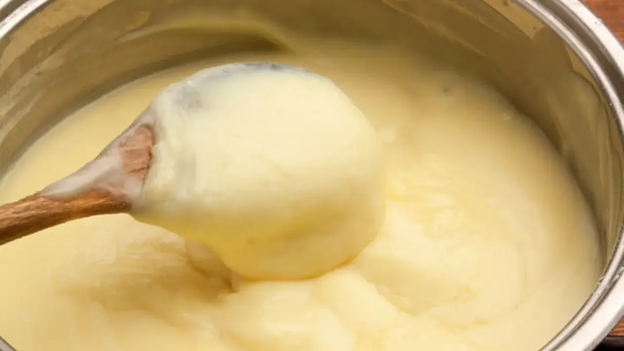 Une cuillère en bois remue une crème pâtissière maison onctueuse dans une casserole.