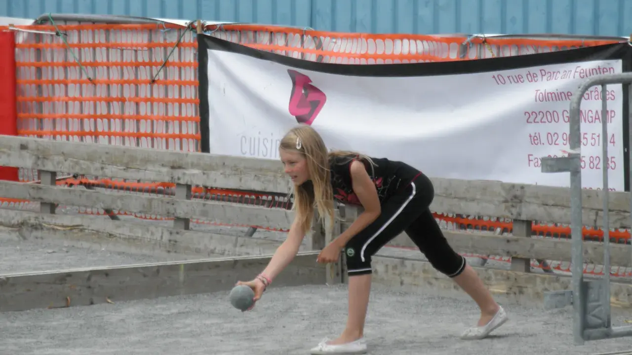 Jeune fille lançant une boule sur un terrain de pétanque, peut-être pour une partie de boule bretonne.