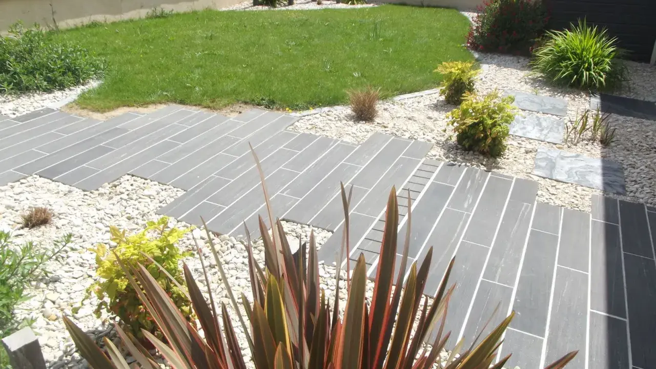 Chemin en dalles grises et gravier blanc, pelouse verte et plantes décoratives. Un jardin facile d'entretien.