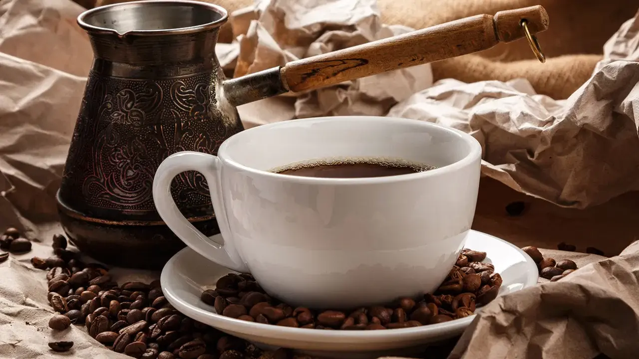 Eine Tasse heißer Espresso Mokka, umgeben von gerösteten Kaffeebohnen und einer traditionellen Mokkakanne.