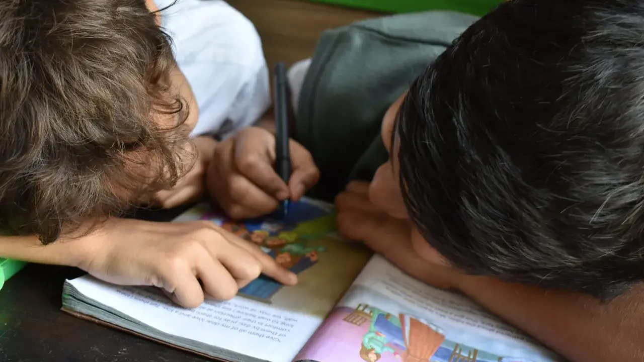 Due bambini studiano insieme, uno scrive mentre l'altro indica il libro. Un esempio di peer learning.