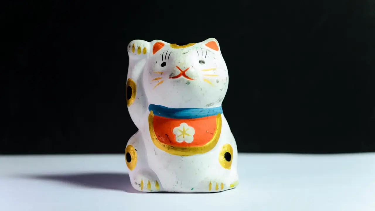 Maneki-neko blanco con detalles dorados y flor, ideal para feng shui en casa para la prosperidad.