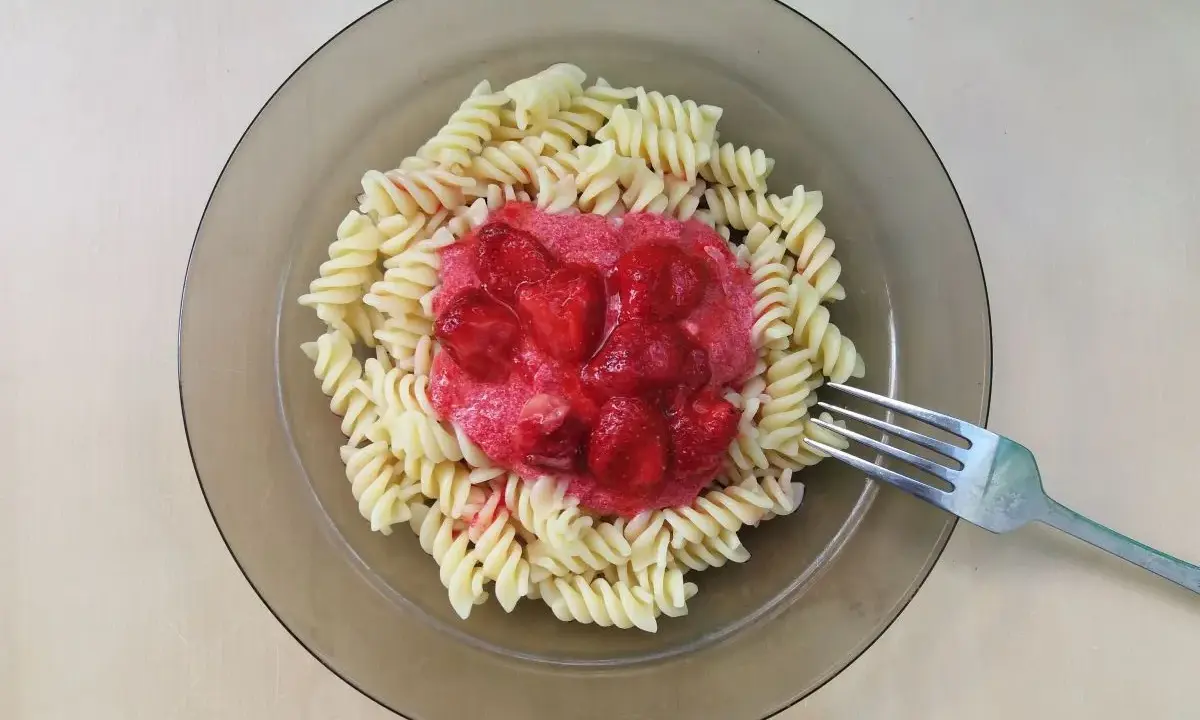 Makaron z truskawkami na talerzu, z widelcem obok.