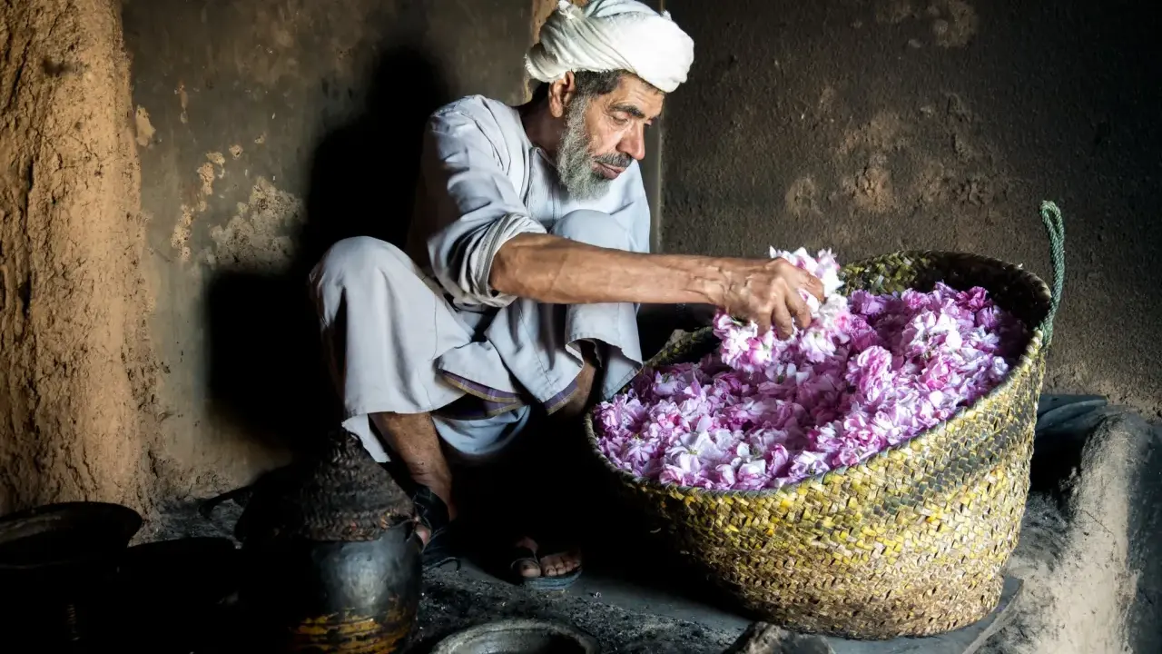 Ein Mann mit Turban und Bart sortiert duftende Blüten in einem Korb. Ein Einblick in die omanische Kultur und traditionelle Handwerkskunst.