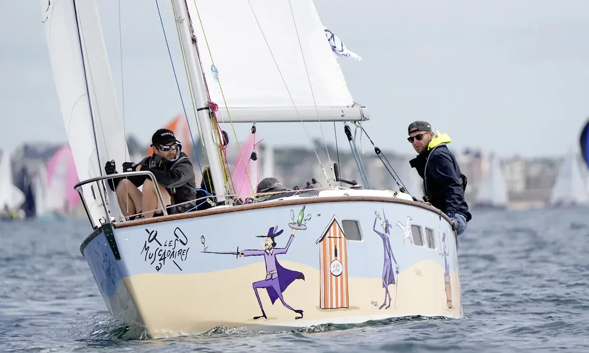Un bateau muscadet décoré de personnages fantaisistes navigue sur l'eau, avec deux hommes à bord.