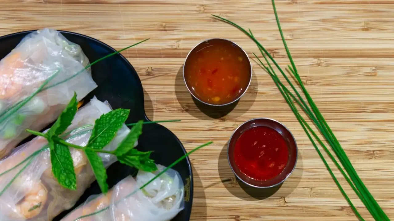 Rouleaux de printemps frais sur une assiette noire, accompagnés de deux sauces : une sauce aigre douce orangée et une sauce rouge.