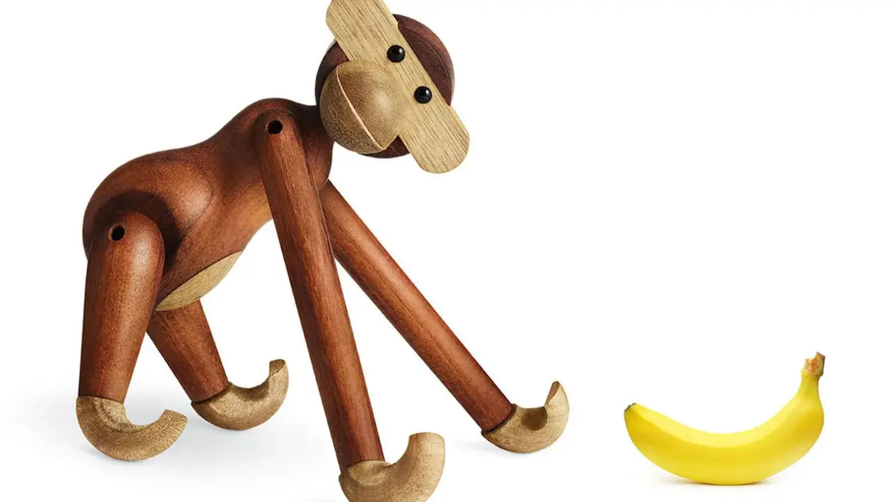 En träapa från Kay Bojesen tittar nyfiket på en banan. Olika kay bojesen apa storlekar finns tillgängliga.