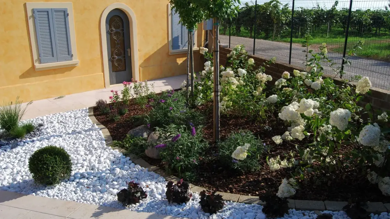 Ingresso esterno di una villetta con ghiaia bianca, piante fiorite e un vialetto. Belle idee per l'esterno della casa.