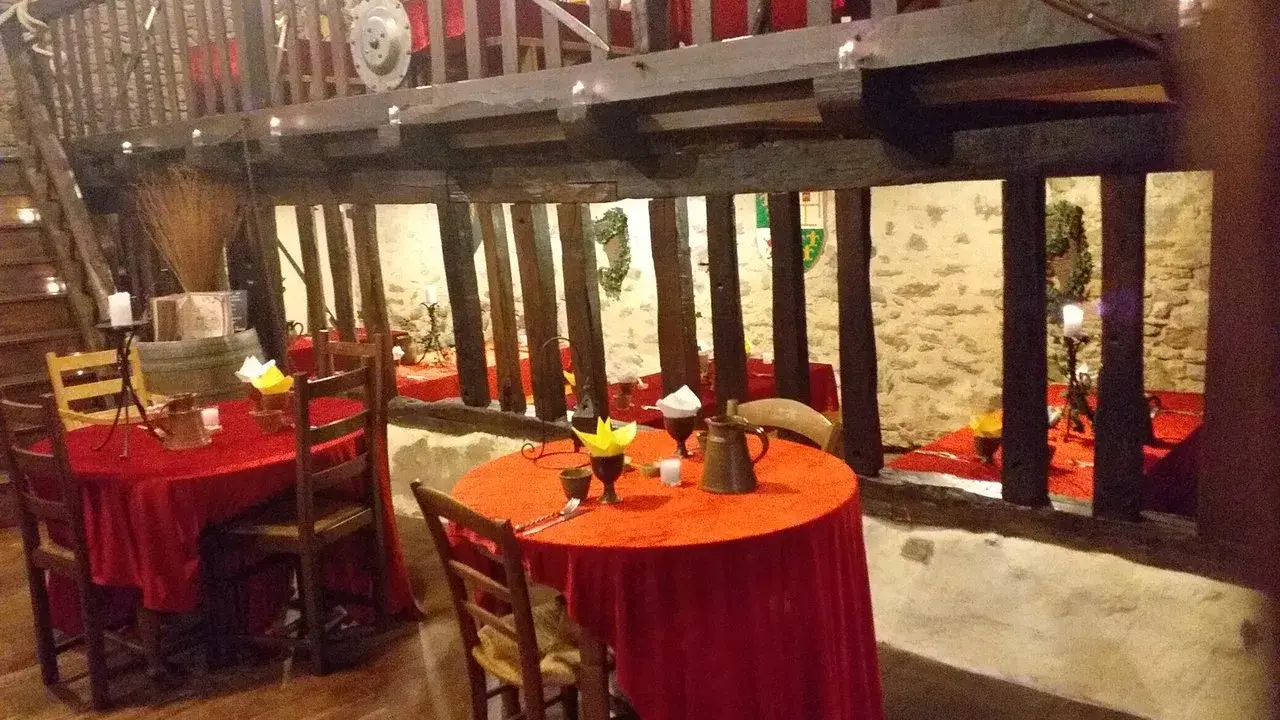 Ambiance d'une auberge moyen âge avec tables dressées de nappes rouges, poutres apparentes et murs en pierre.