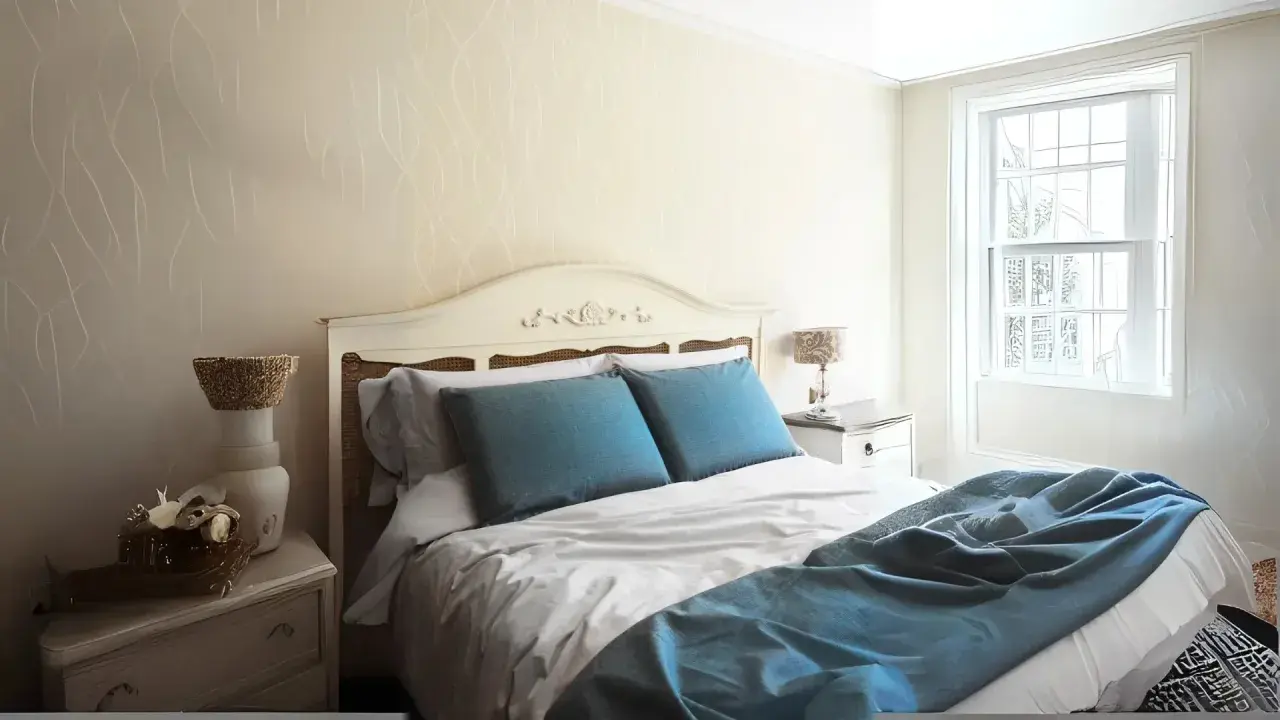 Habitación con cama matrimonial, almohadas azules y manta a juego. Las medidas de camas varían, pero esta parece cómoda.