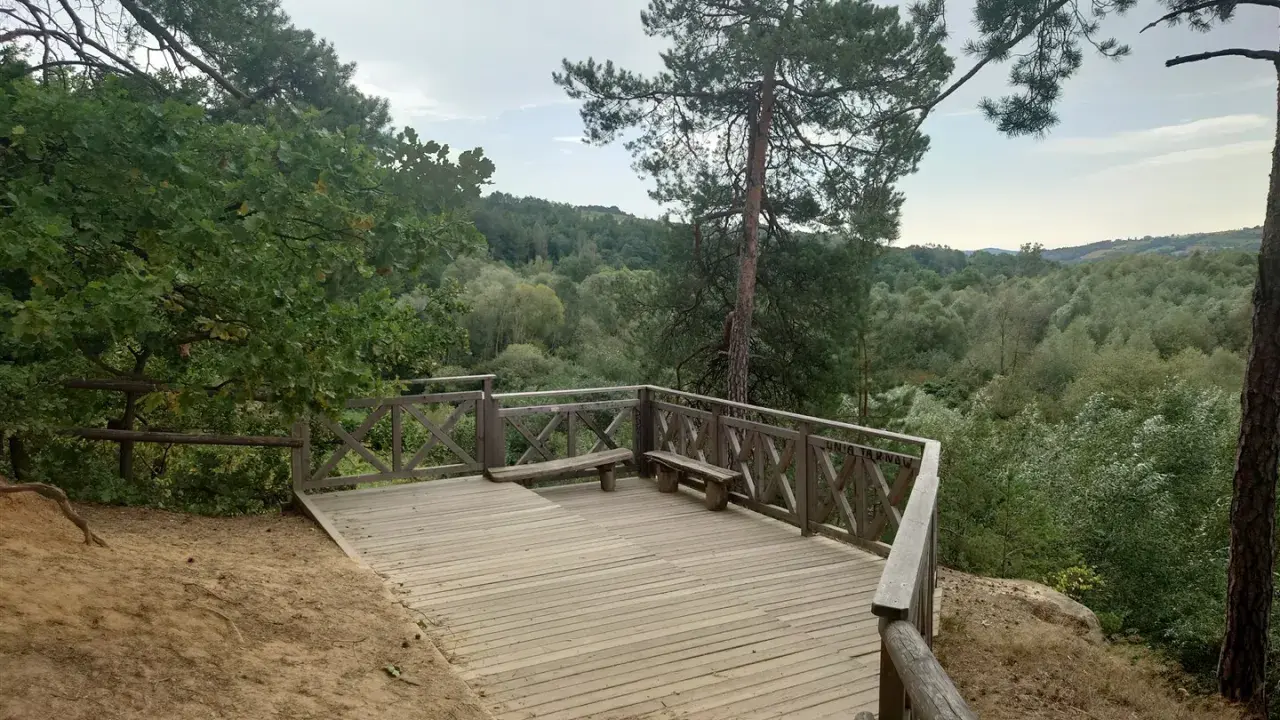 Drewniany taras widokowy z ławką w skalnym mieście Ciężkowice. Widok na zalesione wzgórza.