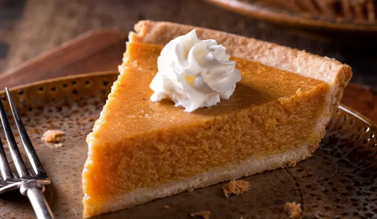 Kawałek pysznego pumpkin pie z bitą śmietaną na talerzu, gotowy do zjedzenia.