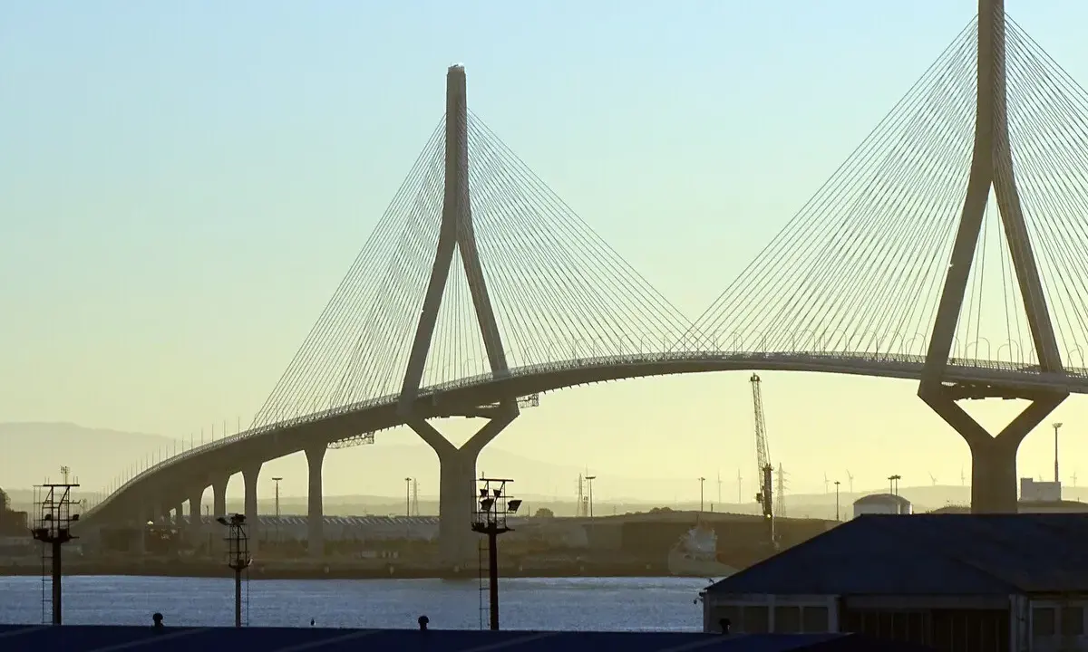 El imponente puente de Cádiz se alza sobre el agua, con sus cables tensos y pilares icónicos contra un cielo despejado.