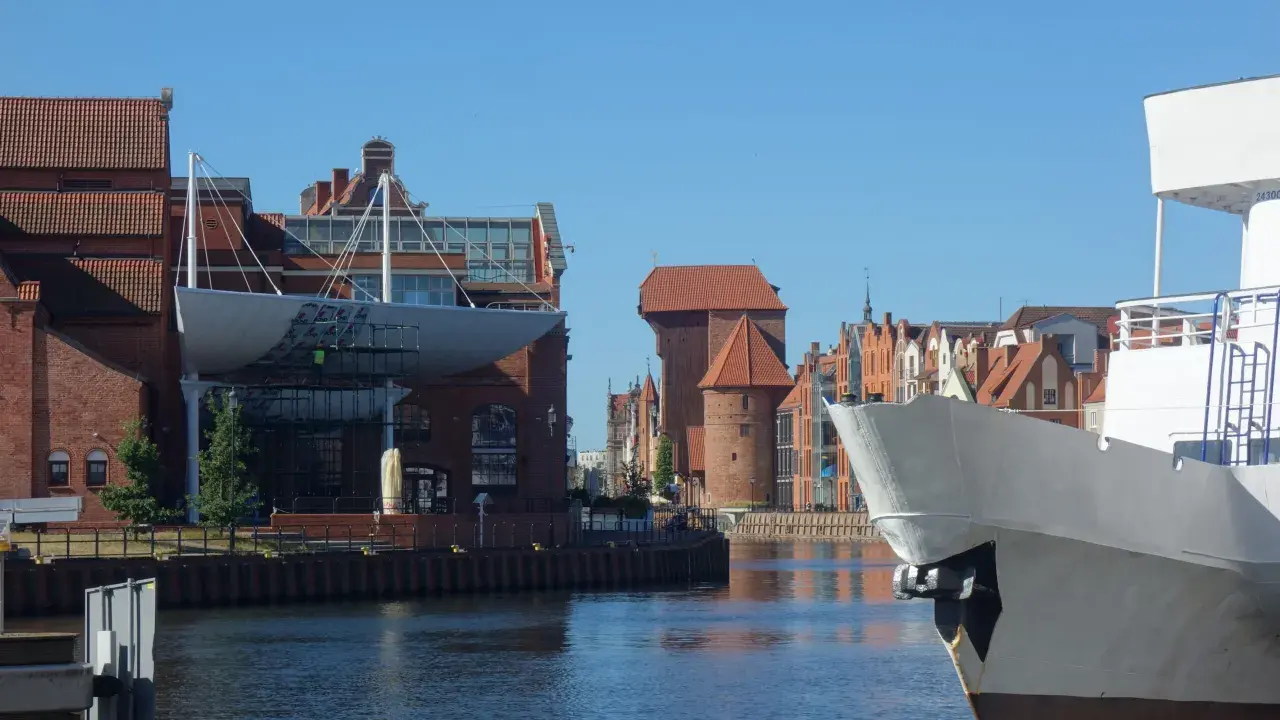 Widok na Motławę w Gdańsku. Na pierwszym planie biały dziób statku, w tle zabytkowe kamieniczki i Żuraw. Gdańsk starówka zachwyca.
