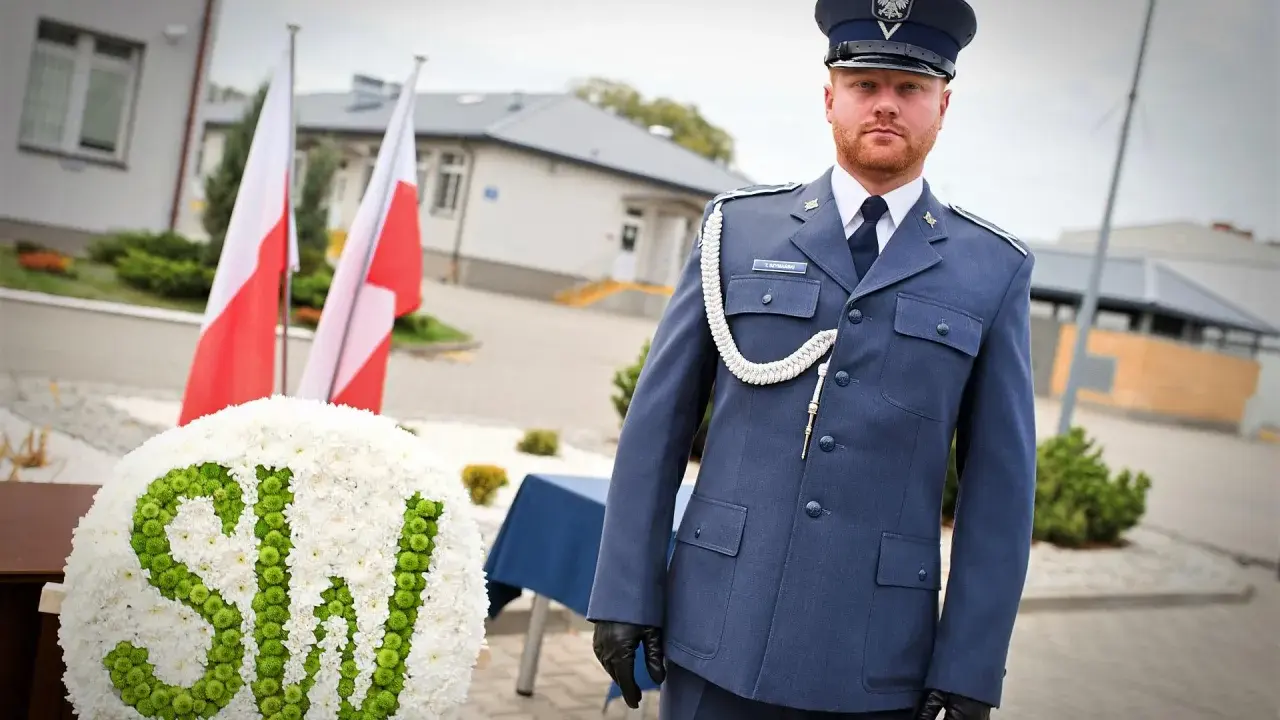 Mężczyzna w mundurze galowym SW, biało-zielony wieniec z napisem SW, polskie flagi.