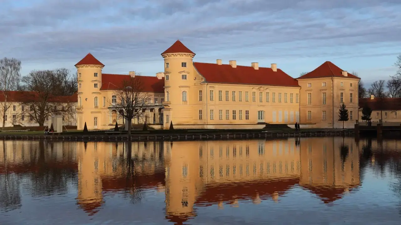 Das Schloss Rheinsberg spiegelt sich im Wasser. Die historische Altstadt von Rheinsberg zeigt sich von ihrer schönsten Seite.