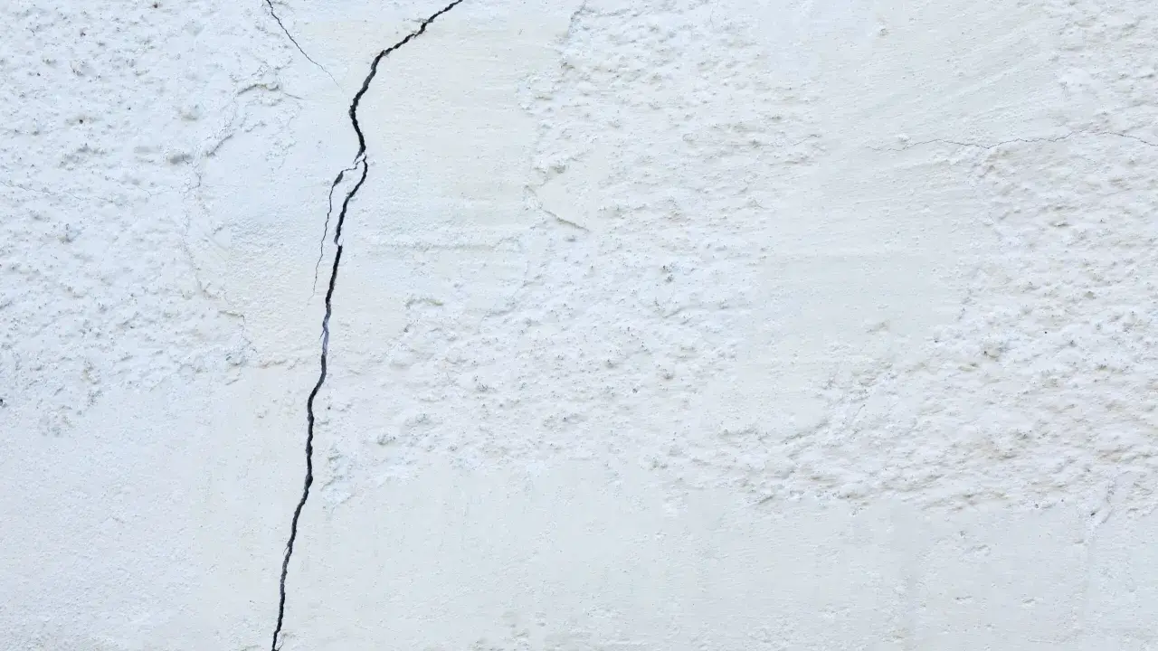 Un muro de casa blanco con una grieta oscura que lo atraviesa. La textura es rugosa y desigual.