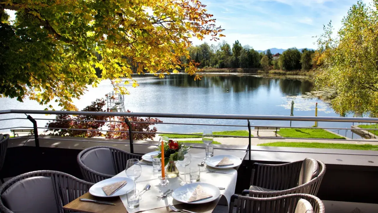 Gedeckter Tisch mit Blick auf einen See und Herbstlaub.